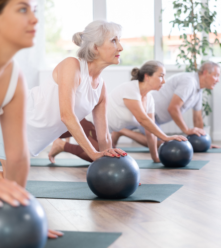 Group of mature active people doing soft ball exercises during group pilates class in fitness studio